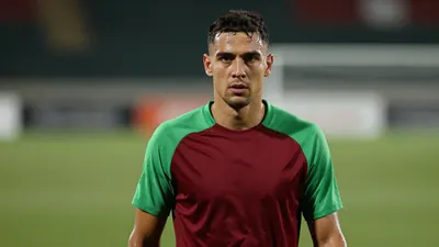 A mid-30s anonymous forward, athletic build, waist-up, intense gaze, dark red and green home training top with smooth...