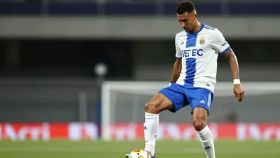 A photorealistic image of a Le Mans FC player in a white jersey with a blue stripe, a blue short, and a pair of white...