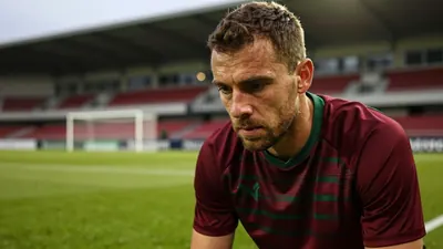 A close-up portrait of a 35-year-old male football coach with a rugged build, wearing a plain dark red and green striped...