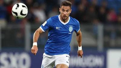 A tight shot of a Le Mans FC player in a blue jersey with white shorts, running with the ball, a positive and dynamic...