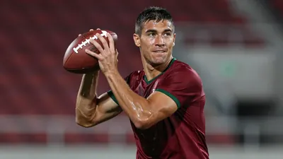 Mid-30s muscular forward, waist-up, sweat-glazed dark red shirt with subtle green trim, plain cotton texture, face...