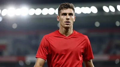 A mid-30s anonymous Le Mans FC midfielder in a solid red jersey, waist-up, focused expression, background blurred stadium...