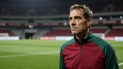 A 35-year-old, 5'10" athletic coach in a plain, dark red and green polyester training top, standing on the Stade...