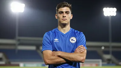 Photorealistic portrait of a 22-year-old central defender in a solid blue jersey, standing confidently with arms crossed...