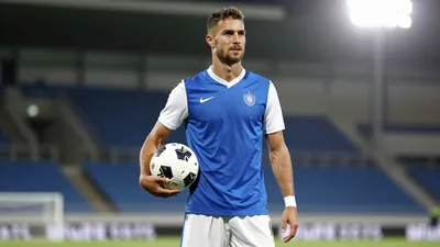 A photorealistic image of a Le Mans FC player, wearing a blue jersey with white sleeves and a white kit, holding a...