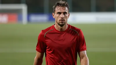 Mid-30s Le Mans FC forward, athletic build, waist-up, intense gaze, dark red shirt with subtle green piping across the...