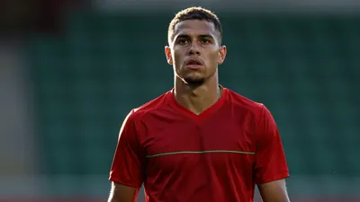 A focused, waist-up portrait of a 24-year-old Le Mans FC midfielder, muscular build, intense eyes, sweat glistening on...