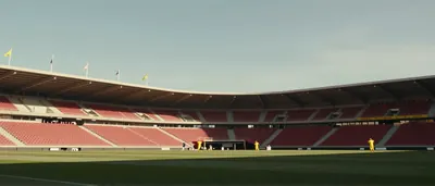 A hyper-realistic editorial shot of a packed Stade du Mans, sea of red and black scarves waving as a lone forward in a...
