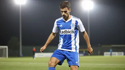 A 24-year-old anonymous left-back in a Le Mans FC kit (blue and white) with a white shirt and blue shorts, playing a ball...