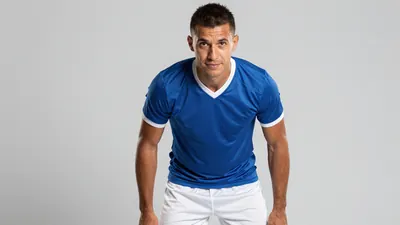 A 30-year-old male player with a strong build, wearing a blue jersey and white shorts, with a determined expression...